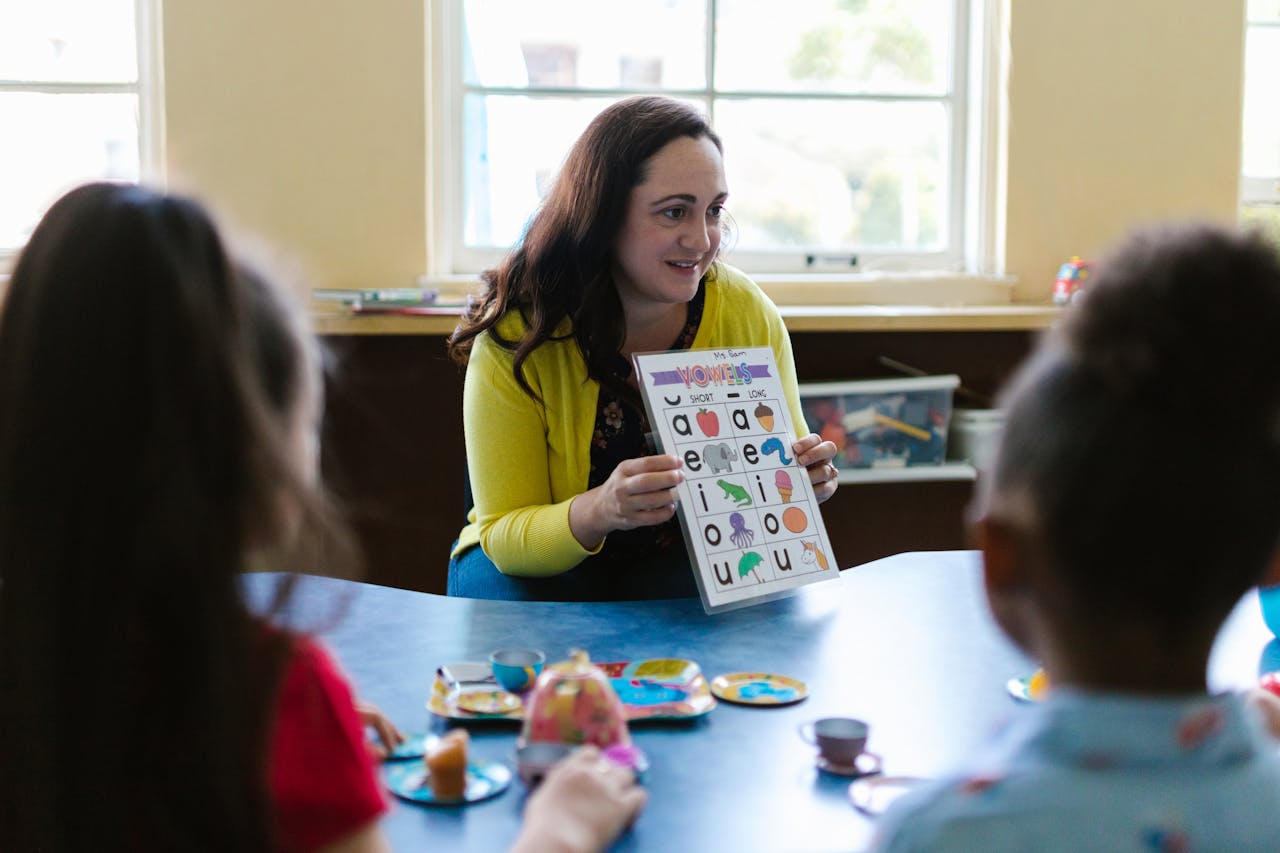 Teacher engaging young children in a fun learning activity with phonics chart in a classroom setting.
